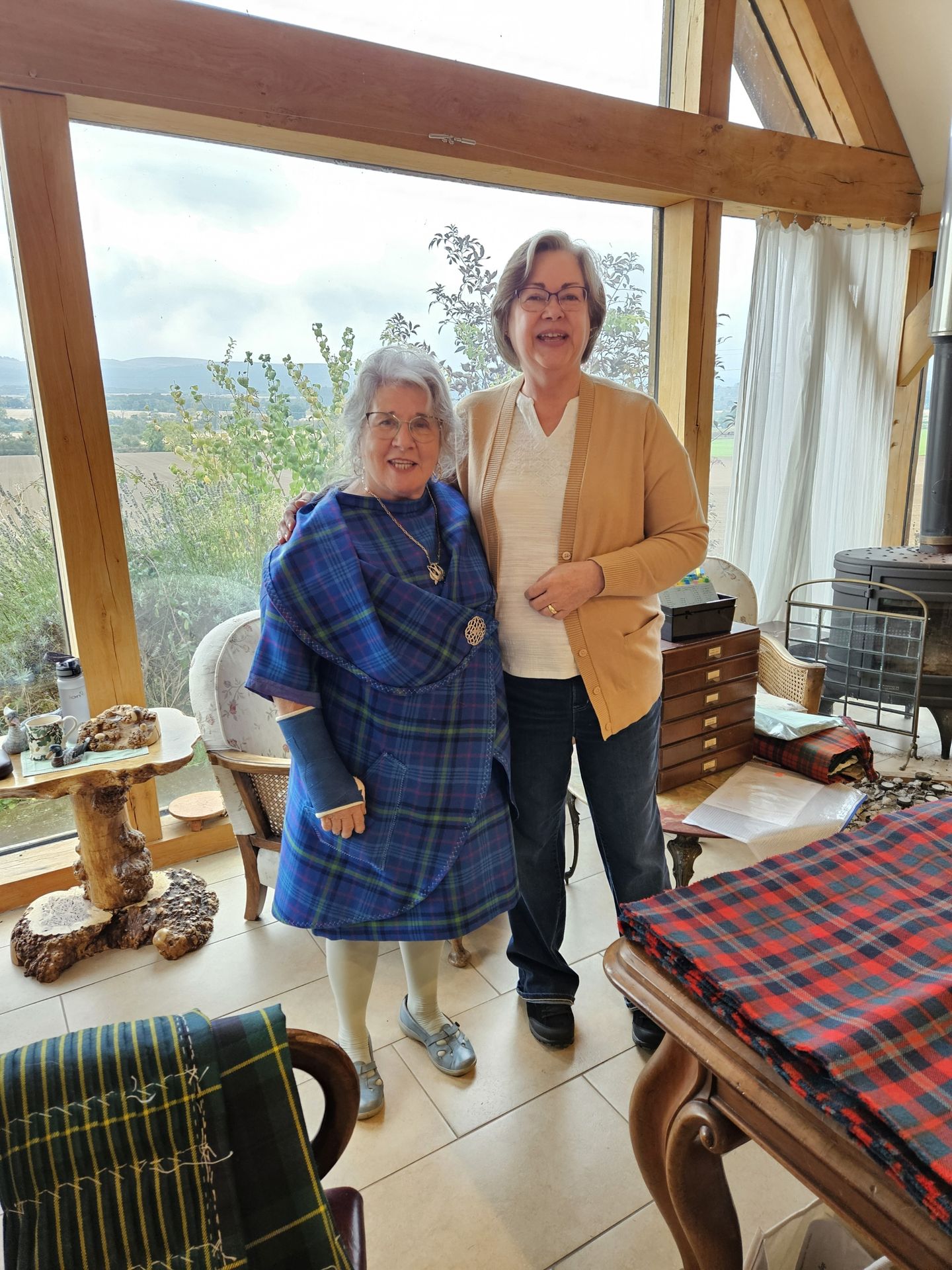 Several students at the College of Master Kilt Tailors are congregating around the stitching table and hearth as they visit Marion, the founder of the College.