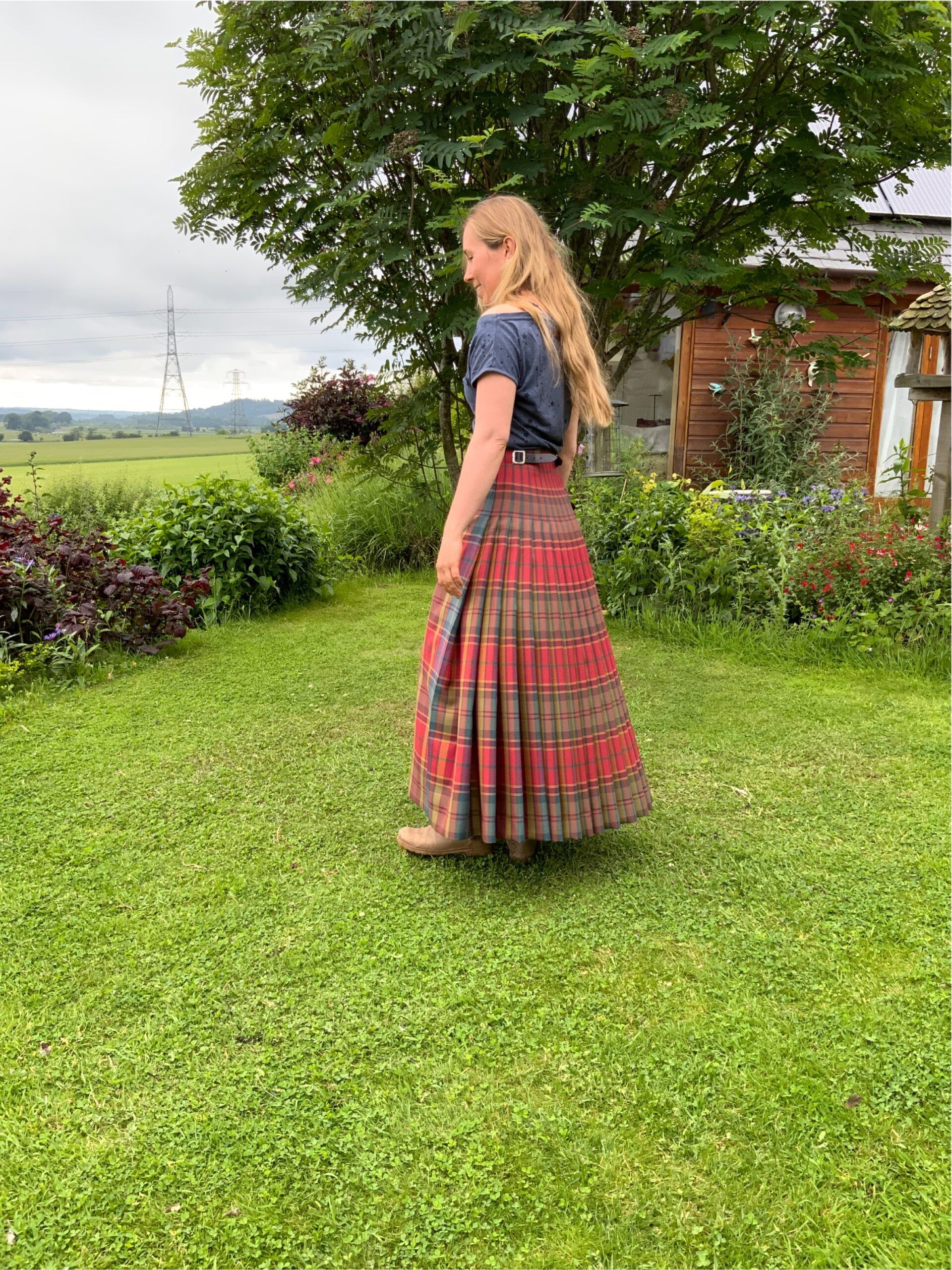 A woman wearing a traditionally tailored long kilt in red, standing on the lawn at The College of Master Kilt Tailors.